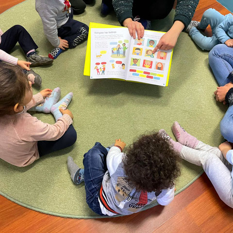 Bambini seduti in cerchio mentre l&rsquo;educatrice legge un libro illustrato